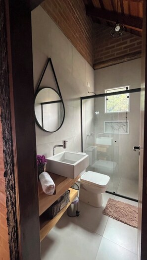 Une salle de bain moderne avec une douche à l’italienne en verre, un miroir rond et un lavabo blanc.
