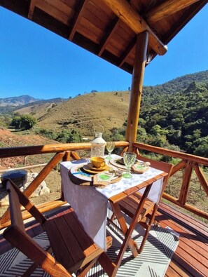Une terrasse en bois avec une table dressée pour le repas, offrant une vue sur un paysage vallonné.
