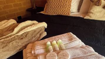 A neatly made bed with a black bedspread, a woven throw blanket, and a set of toiletries including two bottles of shampoo and conditioner, and a bottle of lotion.