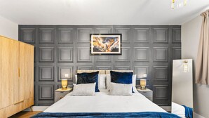 Un dormitorio moderno con una cama grande, paredes revestidas de color gris, dos mesitas de noche con lámparas y un armario de madera.