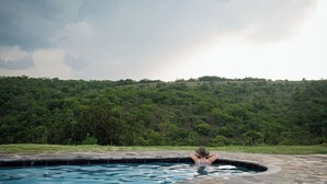 A person relaxing in a swimming pool with a lush green hillside in the background. - Matatane Wilderness Camp (Babanango Game Reserve)