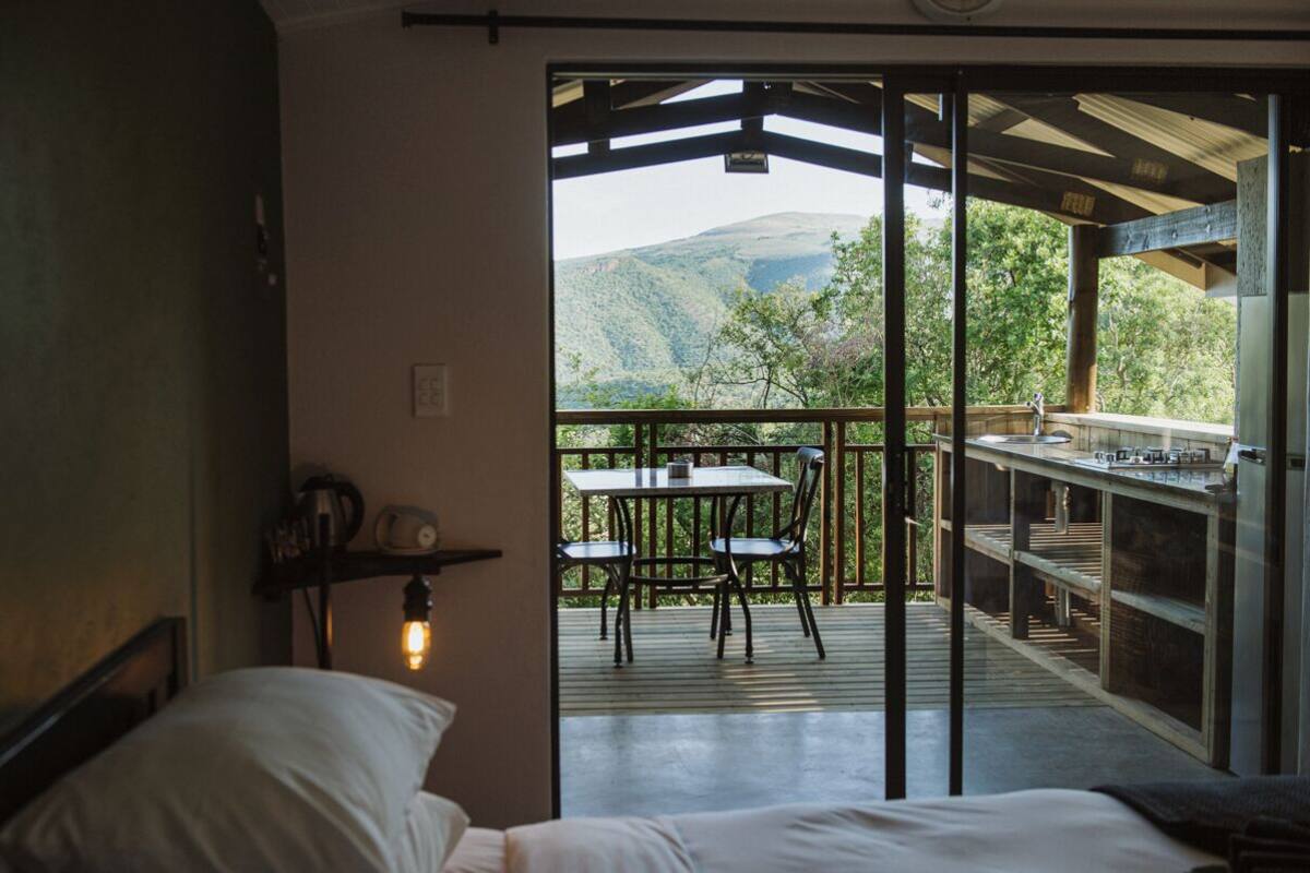 Un dormitorio con cama, mesita de noche y una mesa con sillas. Cuenta con un balcón con mesa y sillas, y vistas a las montañas.
