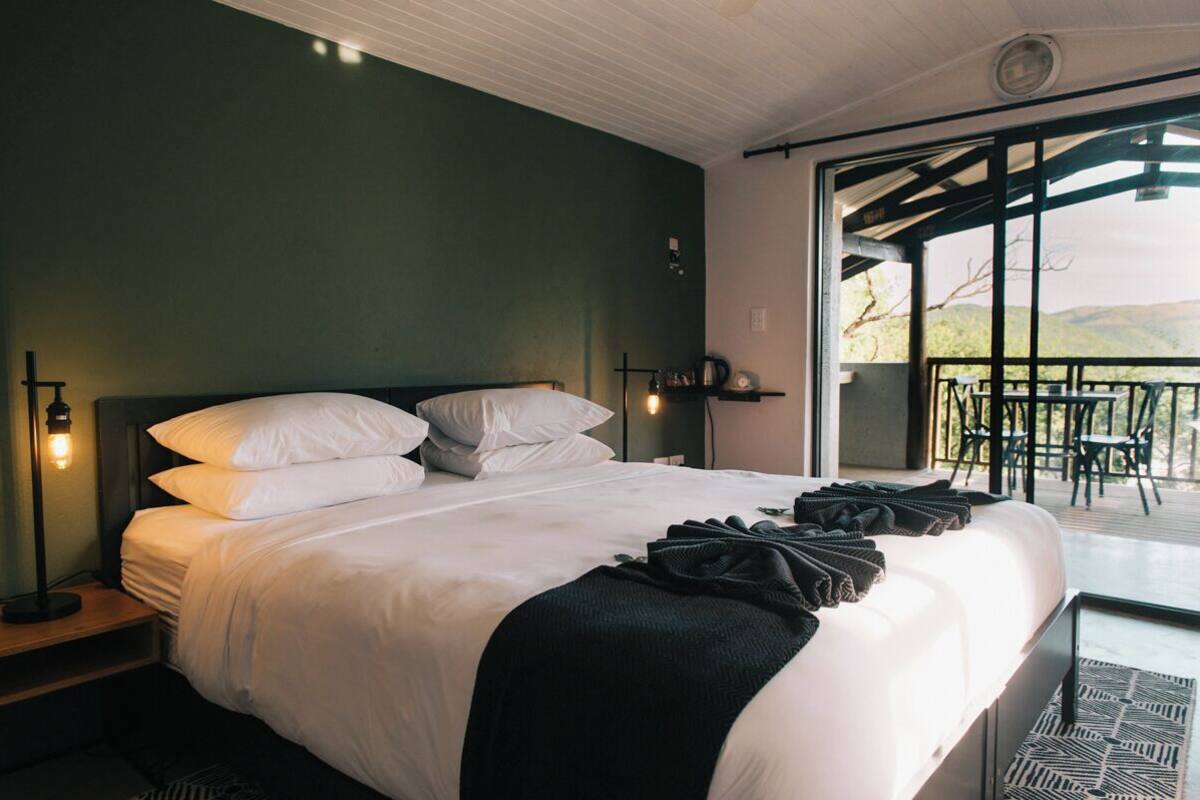 Un dormitorio con una cama grande, una mesita de noche, una lámpara y vistas a un patio exterior con sillas y una mesa.