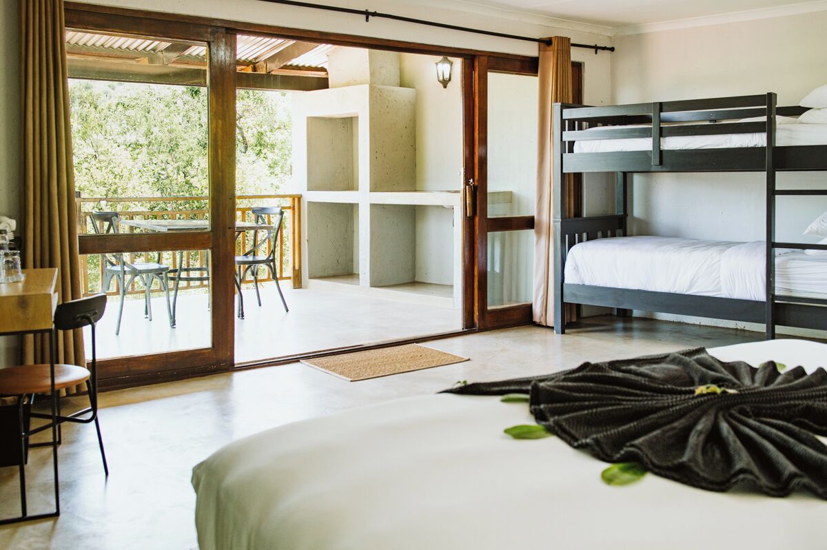Een hotelkamer met een stapelbed, een bureau met stoel en uitzicht op een buitengebied met tafels en stoelen.