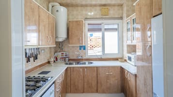 Een keuken met houten kastjes, een gasfornuis, een spoelbak en een raam.