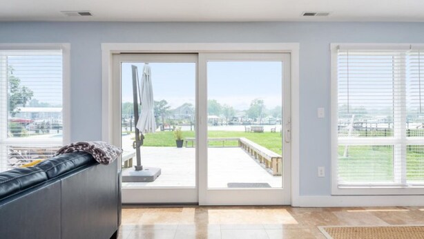 A room with a sliding glass door leading to an outdoor patio, a black leather sofa, and a tiled floor. - Tilghman | Pool | Private Dock | Pet Friendly (Tilghman)
