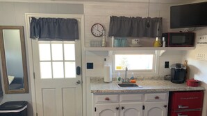 A compact kitchen with white cabinets, a red refrigerator, a microwave, and a clock on the wall. - Cozy cottage (Chincoteague)