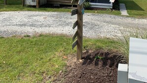 A wooden cabin with a gravel driveway and a wooden signpost with directional signs. - Cozy cottage (Chincoteague)