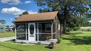 A small wooden cabin with a porch, a large window, and a door with an oval glass panel. - Cozy cottage (Chincoteague)