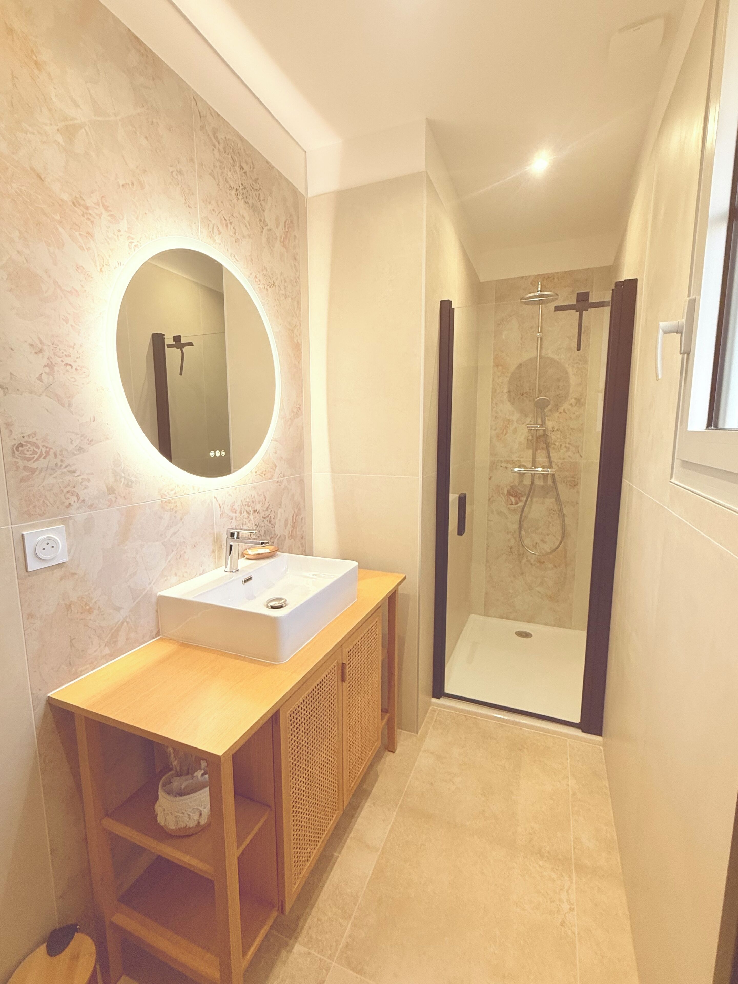 A modern bathroom with a vanity, a round mirror, a shower enclosure, and a small shelf.