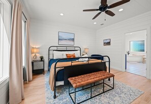 A bedroom with a bed, bench, bedside tables, a ceiling fan, and a bathroom visible through an open door. - Creekside | Disc Golf | Movie Room | Hot Tub (Broken Bow)