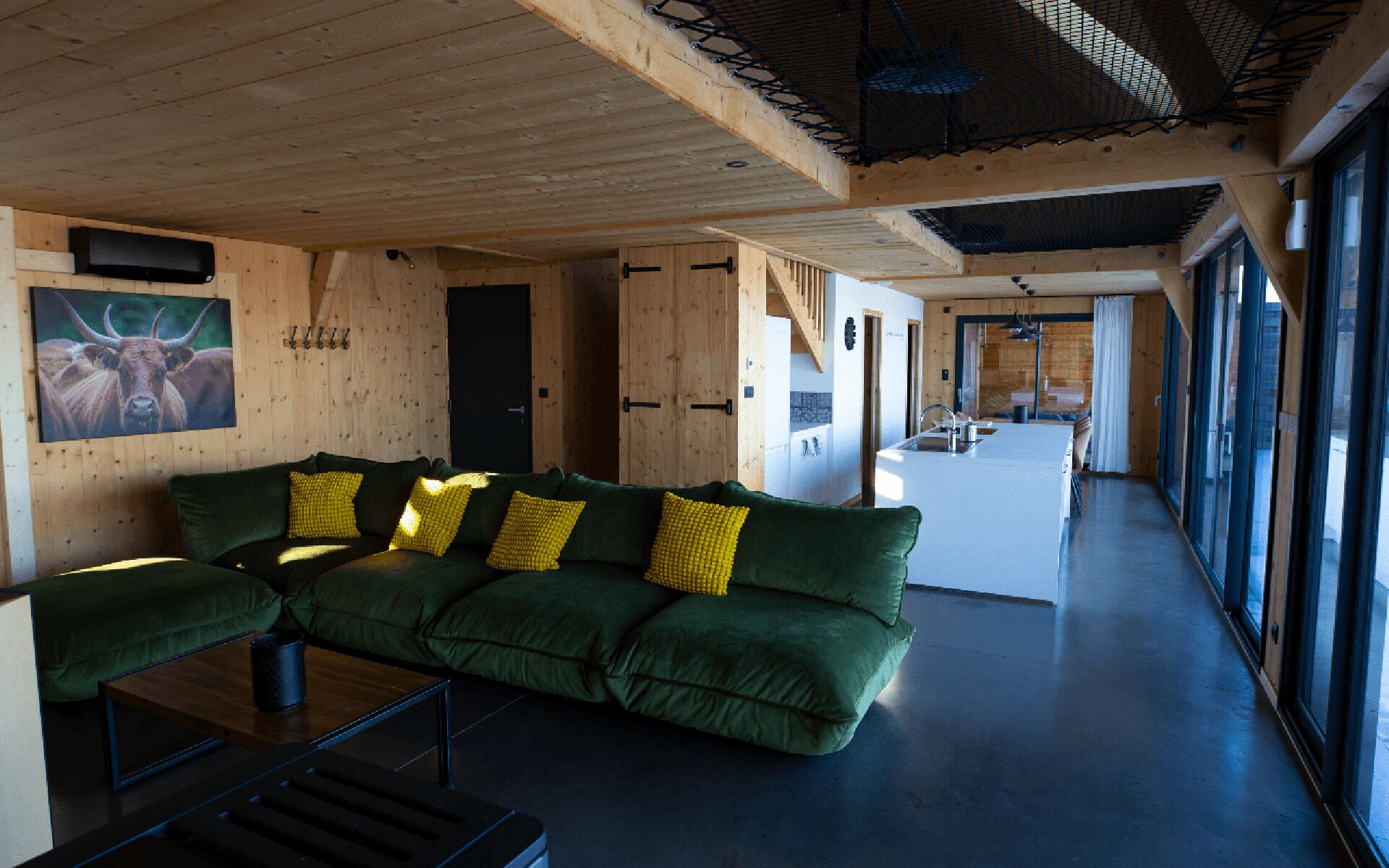 Un interior moderno con sofá verde, paredes de madera y ventanas amplias.