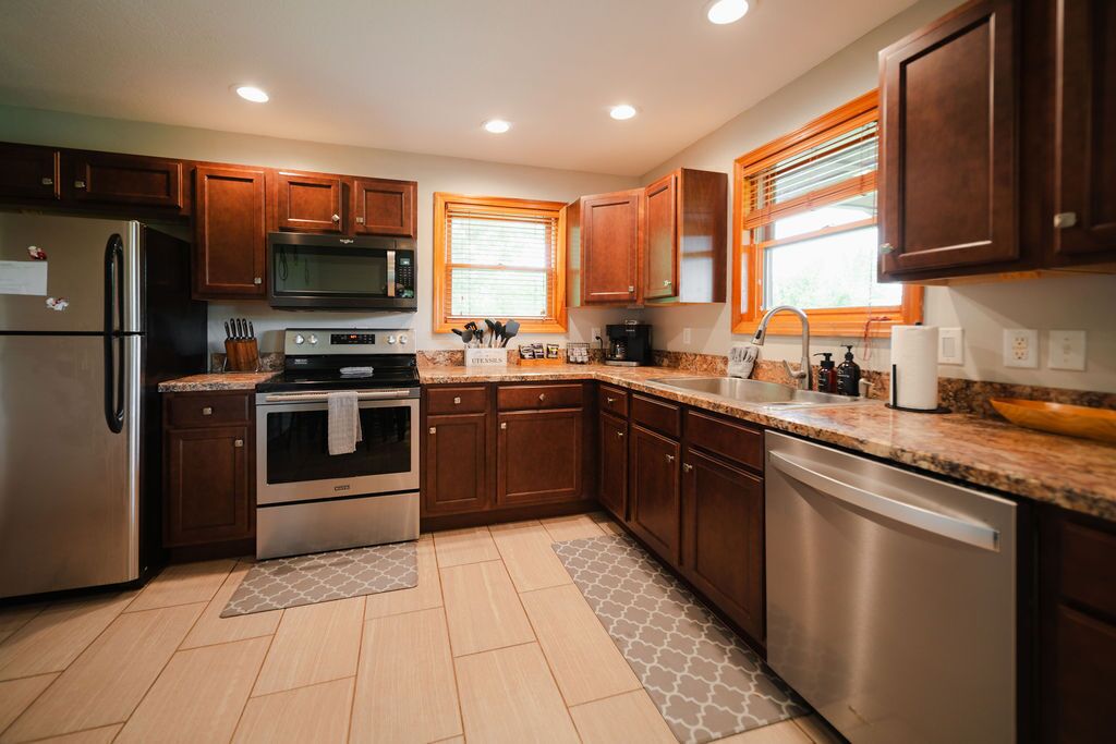 A modern kitchen with wooden cabinets, stainless steel appliances, granite countertops, and a dishwasher.