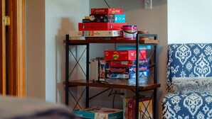 A shelf with various board games and a patterned chair. - The Gathering | Hocking Hills, Hot Tub, Pond (Logan)