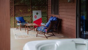 A covered patio area with two rocking chairs, a small table, and a hot tub. - The Gathering | Hocking Hills, Hot Tub, Pond (Logan)