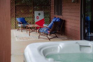 A covered patio area with two rocking chairs, a small table, and a hot tub. - The Gathering | Hocking Hills, Hot Tub, Pond (Logan)