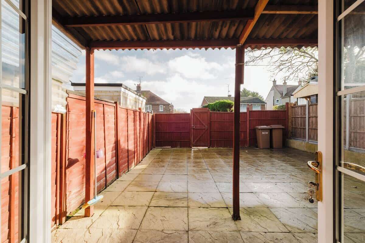 A covered outdoor area with a tiled floor, a wooden fence, and a metal gate.