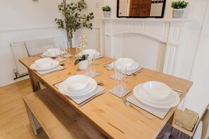 A dining table set with white plates, glasses, and cutlery, with a bench at one end. - Comfortable 3 Bedroom Home Sleeps 5 (Wellingborough)