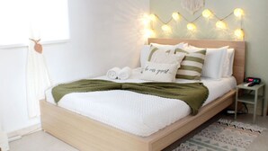 A neatly made bed with a green throw blanket, white pillows, and a sign that says "be our guest." - Newer Gated Condo~Near Airport! 5m Walk to Beach! (San Juan)