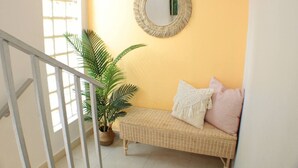 A staircase with a white railing, a wicker bench with cushions, a potted plant, and a round mirror on the wall. - Newer Gated Condo~Near Airport! 5m Walk to Beach! (San Juan)