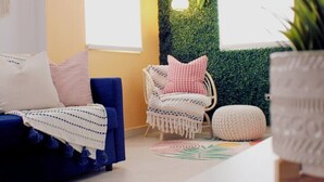 A cozy living room with a blue sofa, a wicker chair with cushions, and a green wall with a hanging light. - Newer Gated Condo~Near Airport! 5m Walk to Beach! (San Juan)
