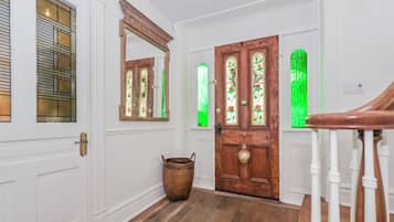 Un pasillo con paredes blancas, suelo de madera, un espejo grande, una puerta de madera con vidrieras y una cesta de mimbre.