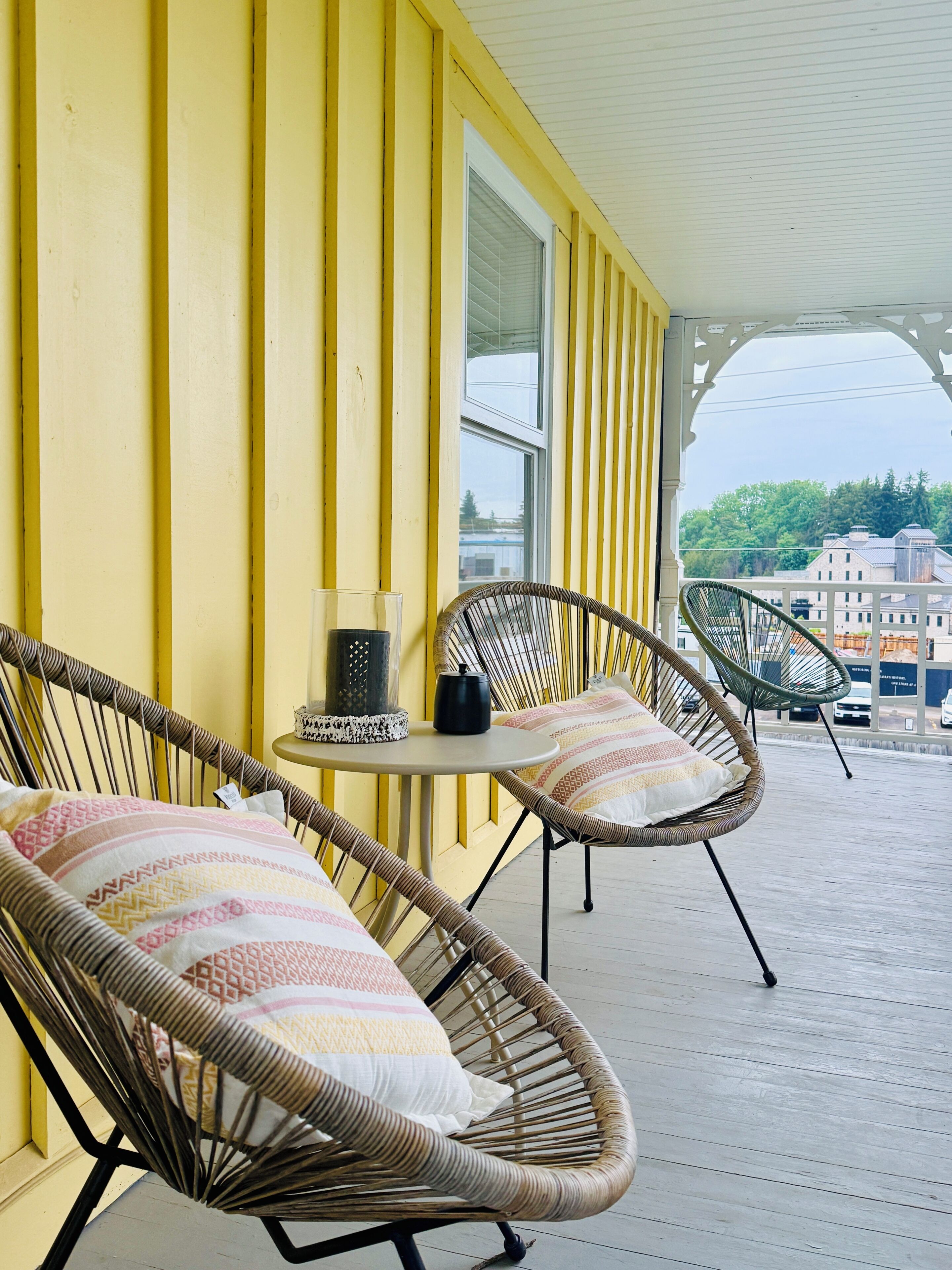 A porch with wicker chairs, a small round table, and a window with blinds.