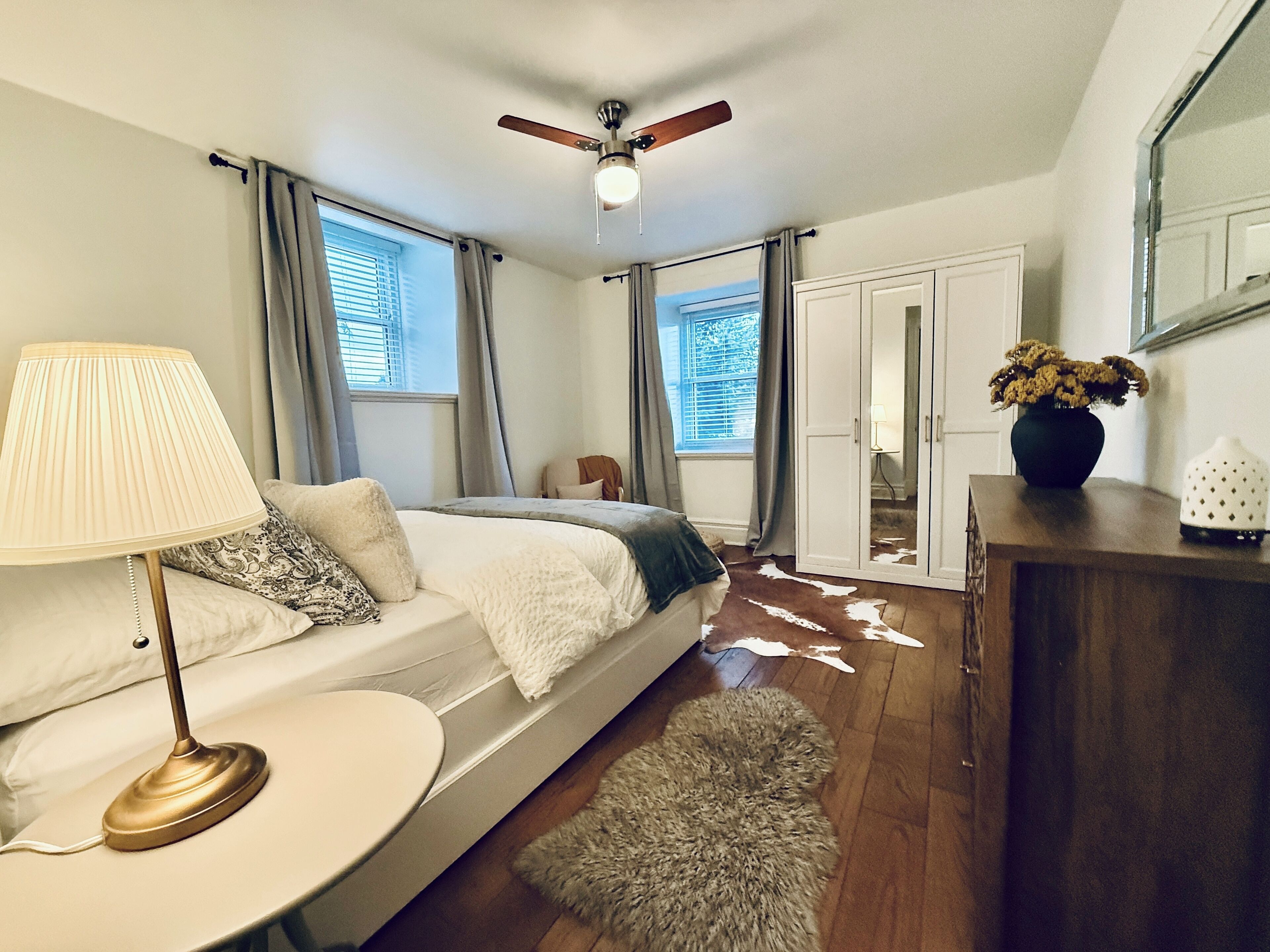 Quarto com cama, mesa de cabeceira, abajur, cômoda, espelho e ventilador de teto.