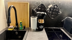 A kitchen with a black sink, a faucet, a bottle of dish soap, and a container with utensils.