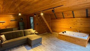 Een gezellig houten blokhut interieur met een hoekbank, een ruime badkuip en een houten plafond.