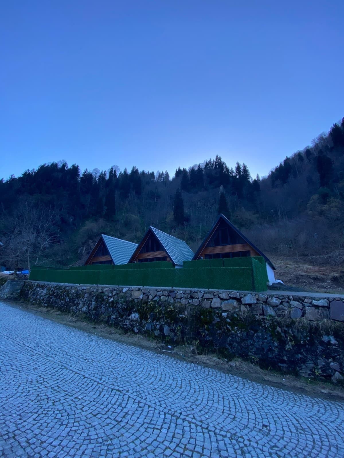 A row of cabins with sloped roofs, surrounded by a stone wall and a cobblestone path.