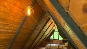 Une chambre confortable située dans les combles, avec des murs en bois, un plafond en pente et un lit simple agrémenté d’oreillers.