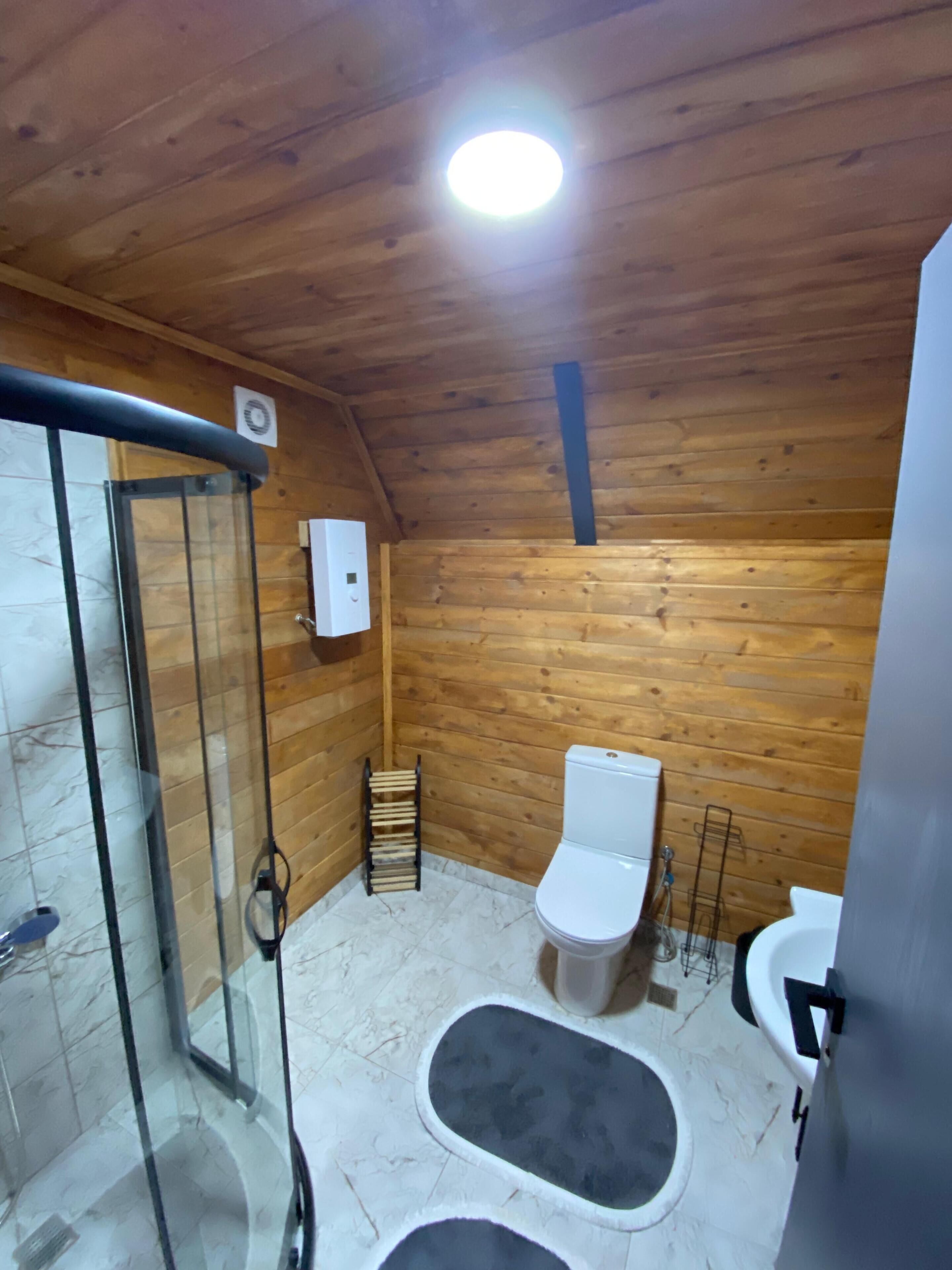 Un baño con paneles de madera, cabina de ducha de vidrio, inodoro y lavamanos.