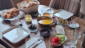 Een ontbijttafel met diverse lekkernijen, een raam met uitzicht op groen en een kamerplant.