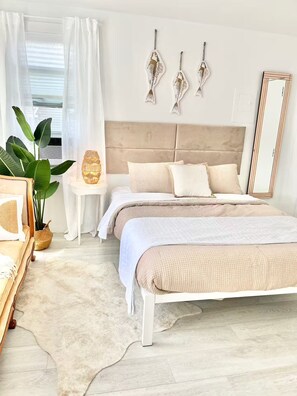 A bedroom with a large bed, a bedside table, a mirror, and a potted plant. - Steps From the Beach Designer Space For 2 (Rockaway Beach)