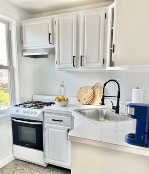 A kitchen with white cabinets, a gas stove, a sink, and a coffee machine. - Steps From the Beach Designer Space For 2 (Rockaway Beach)