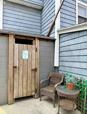 A wooden door with a sign, a wicker chair, and a potted plant in a courtyard. - Steps From the Beach Designer Space For 2 (Rockaway Beach)