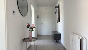 En hall med en rund spegel, ett litet bord med blommor, en bänk och ett element.