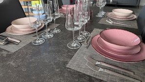 Ett matbord dukat med rosa tallrikar, klara vinglas och silverbestick, i en modern inredning med utsikt över omgivningen.