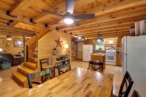 Interior de una cabaña de madera con una mesa de comedor, sillas, una zona de cocina y una escalera.
