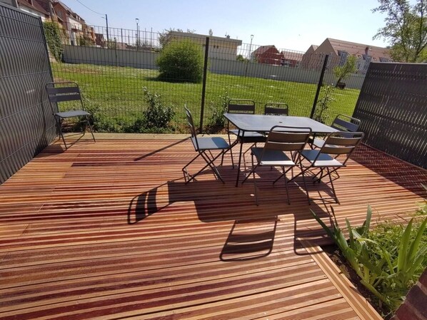 A wooden deck with a table and chairs, surrounded by a metal fence.
