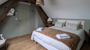 Une chambre avec un plafond en pente, des poutres en bois, un lit recouvert d’une couverture marron, une lampe de chevet et une fenêtre.