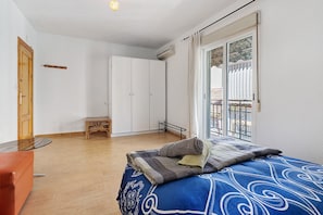 Een slaapkamer met een bed, een houten deur, een kledingkast, een tafeltje en een balkon met een hekwerk.