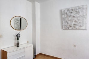 Una habitación con un aparador blanco, un espejo redondo, un florero con plantas y un cuadro abstracto colgado en la pared.