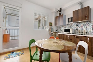 Een keuken met een betegelde achterwand, houten kastjes, een magnetron en een eethoek met een ronde tafel en stoelen.