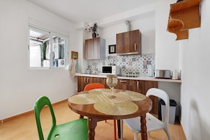 Cocina compacta con armarios de madera, microondas y mesa con sillas.