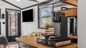 Una cocina moderna con cafetera, encimera de madera y un amplio ventanal con vistas a árboles.