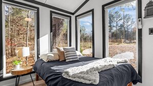 Un dormitorio con una cama grande, varias ventanas y vistas a árboles y una valla.
