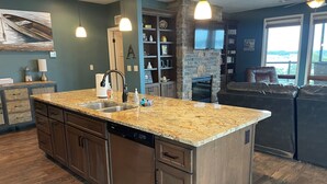 Une cuisine moderne dotée de plans de travail en granit, d’un lave-vaisselle et d’un mur décoratif en pierre.