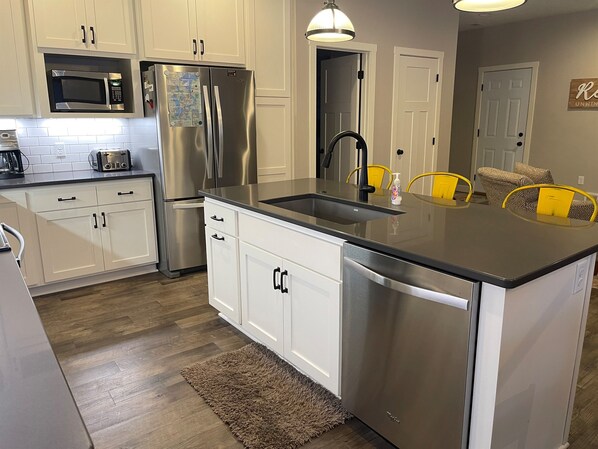 A modern kitchen with white cabinets, stainless steel appliances, a central island with a sink, and yellow chairs.
